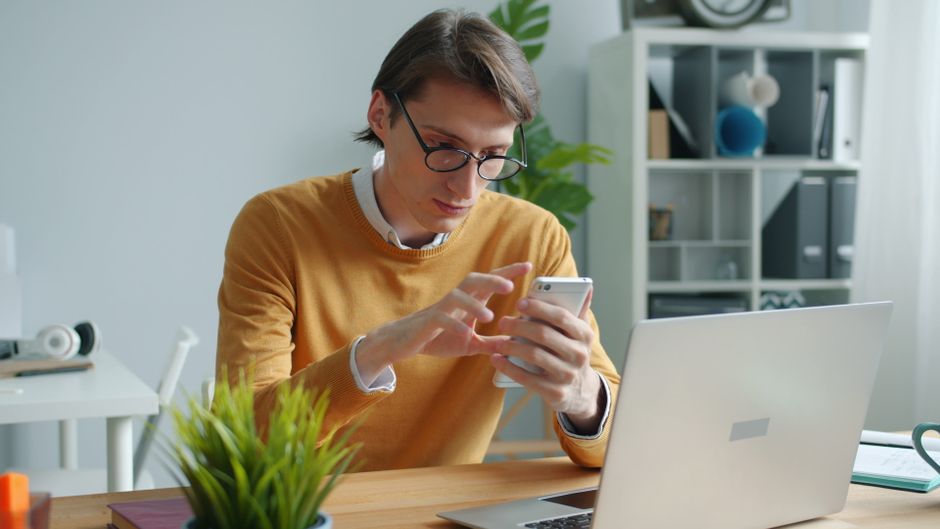 スマートフォンとノートパソコンで状況を確認する人物